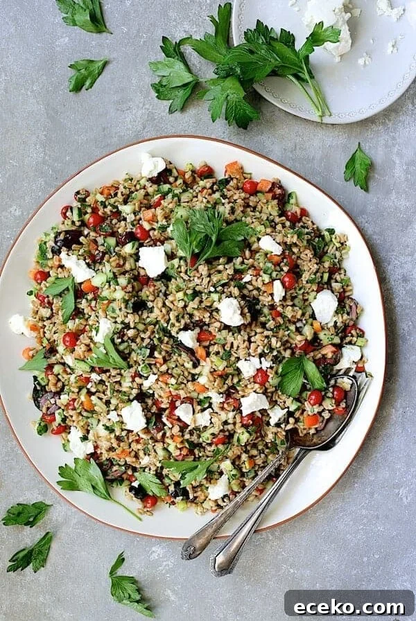Mediterranean Farro Salad on round white platter with serving utensils garnished with parsley.