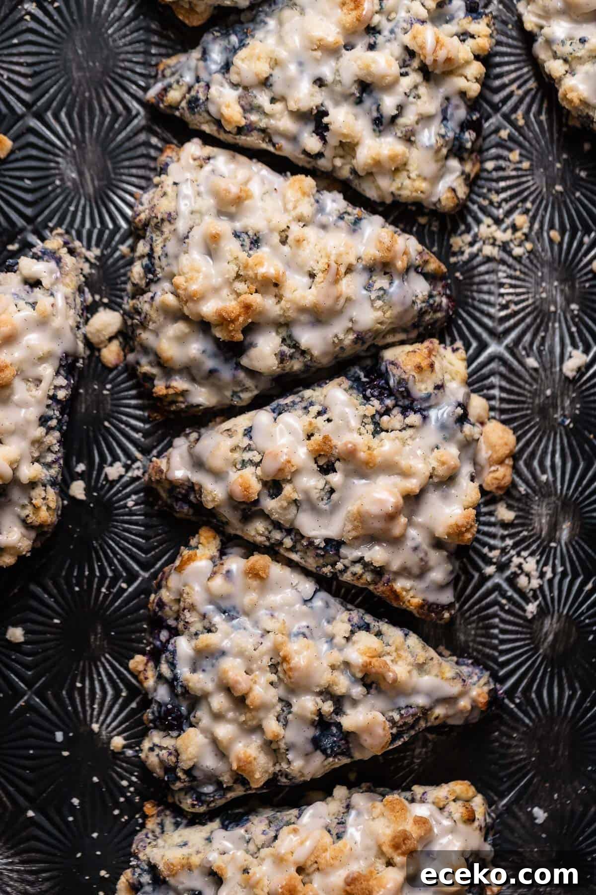 Blueberry scones on a black baking sheet drizzled with vanilla glaze.