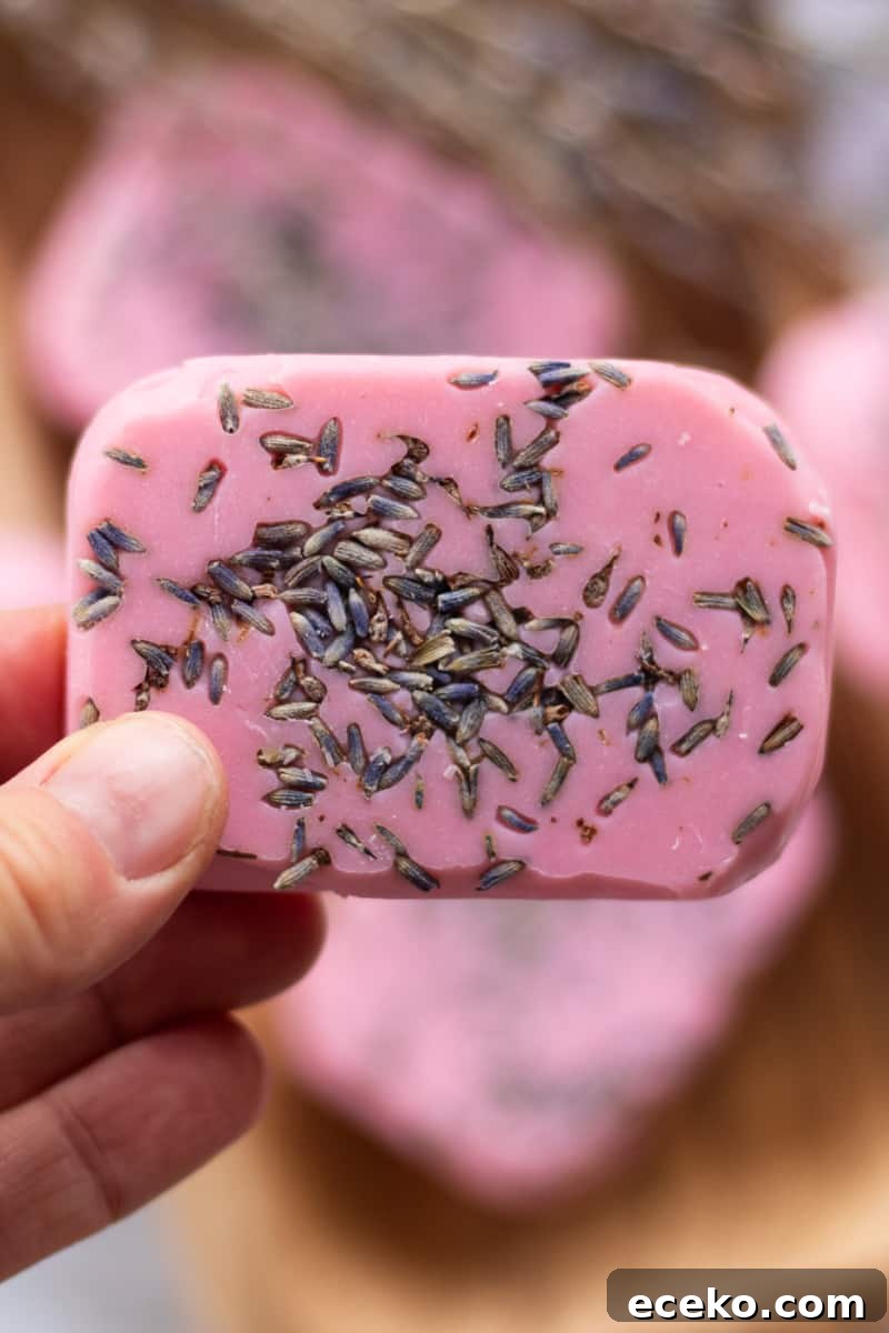 A hand holding a bar of pink soap that has lavender buds pressed into it.