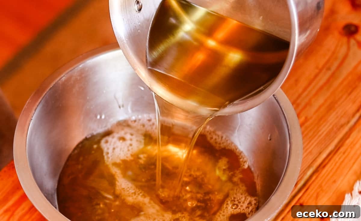 A saucepan filled with melted oils for soap making being poured into a large metal bowl.