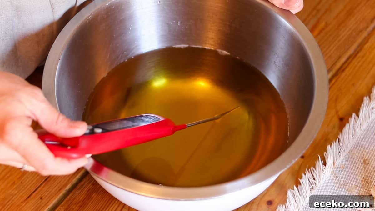 A hand holding a digital thermometer dipped in a bowl of melted oils checking the temperature of the oils.