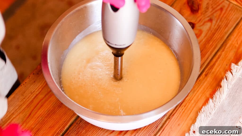 An immersion blender bringing a bowl filled with soap ingredients to a trace.