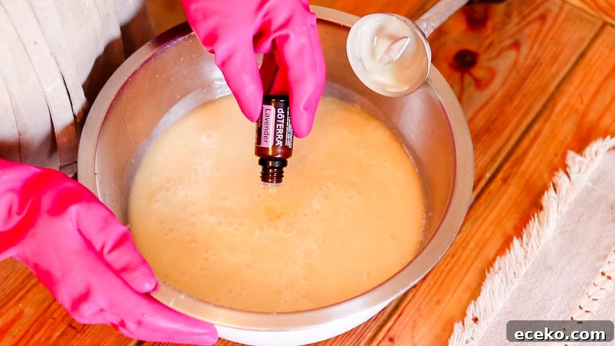 A woman pouring lavender essential oil drops into a large bowl filled with soap batter.