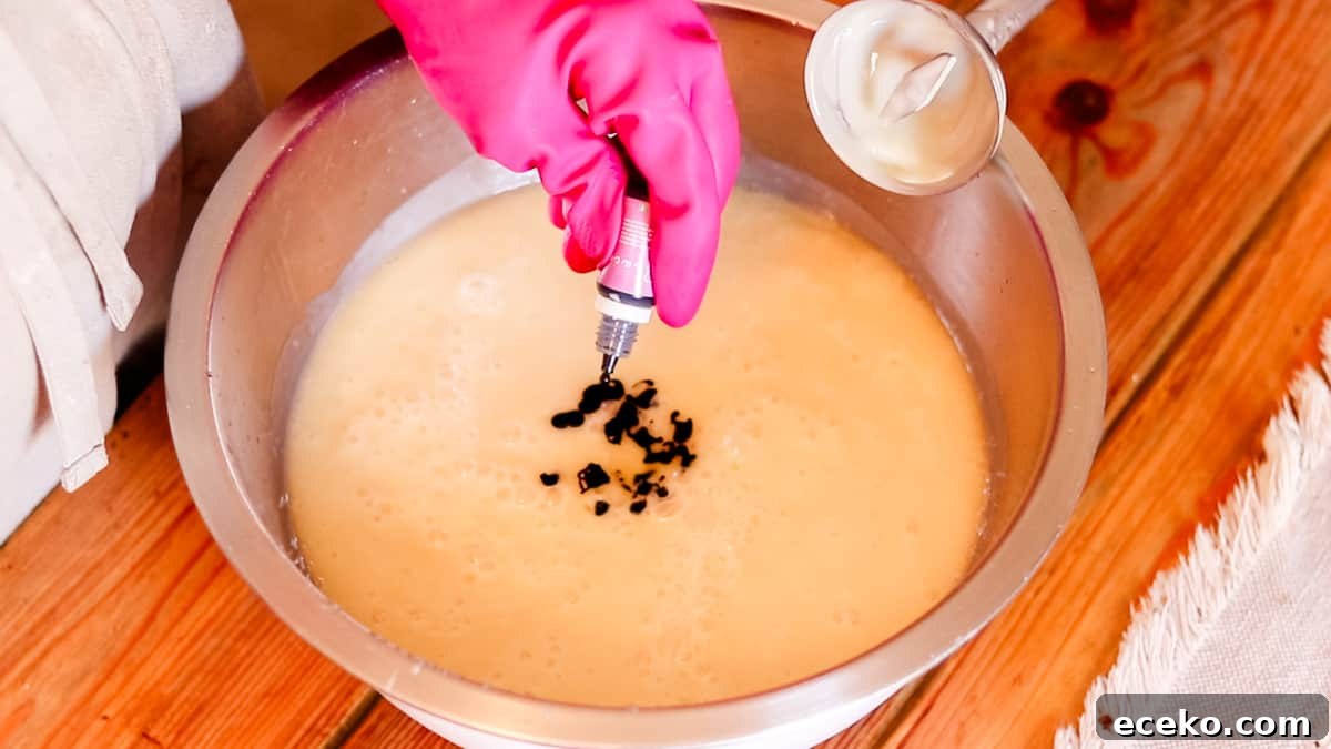 A hand pouring drops of coloring dye into a bowl filled with DIY soap batter.