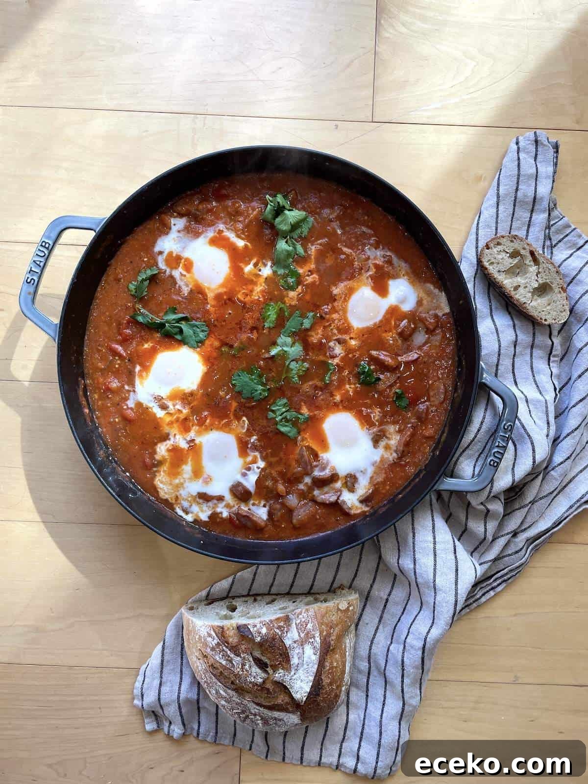 Creole-Style Tomato Shakshuka 2 A pan of creole tomato shakshuka with 5 eggs and a sourdough bread loaf next to it.
