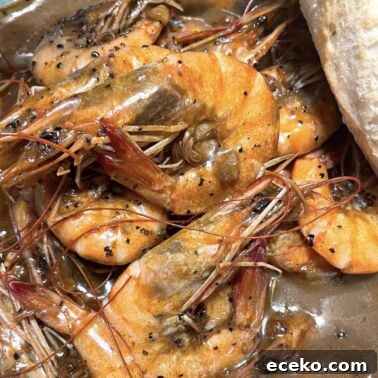 Creole-Style Tomato Shakshuka 7 Cooked BBQ shrimp in a bowl with a loaf of crunchy bread.