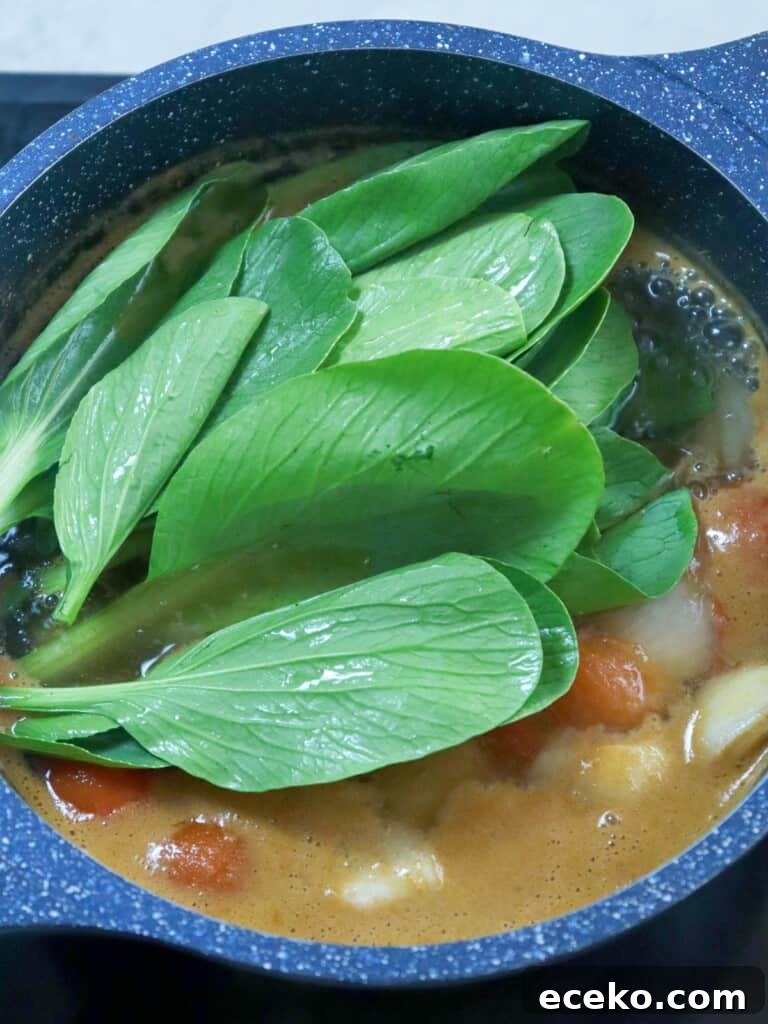 adding bok choy to a pot of sinigang soup