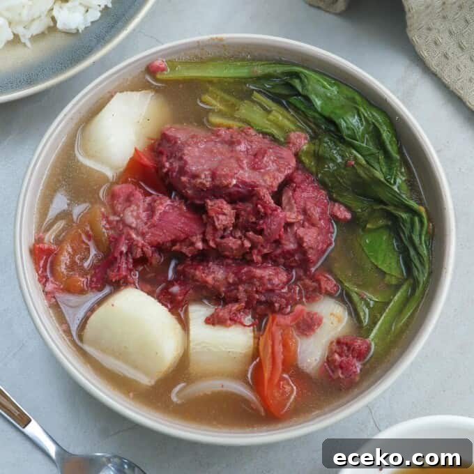 sinigang na corned beef in a white bowl with a plate of rice on the side