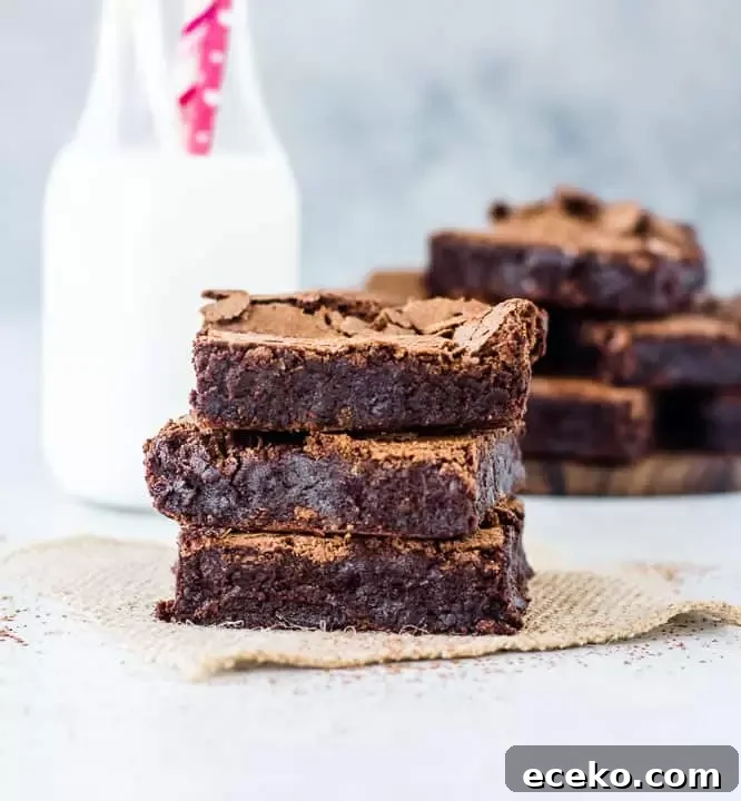 Fudgy Flourless Chocolate Brownies — Moist & Decadent Recipe 6 three flourless brownies stacked on top of each other with milk and more brownies in the background
