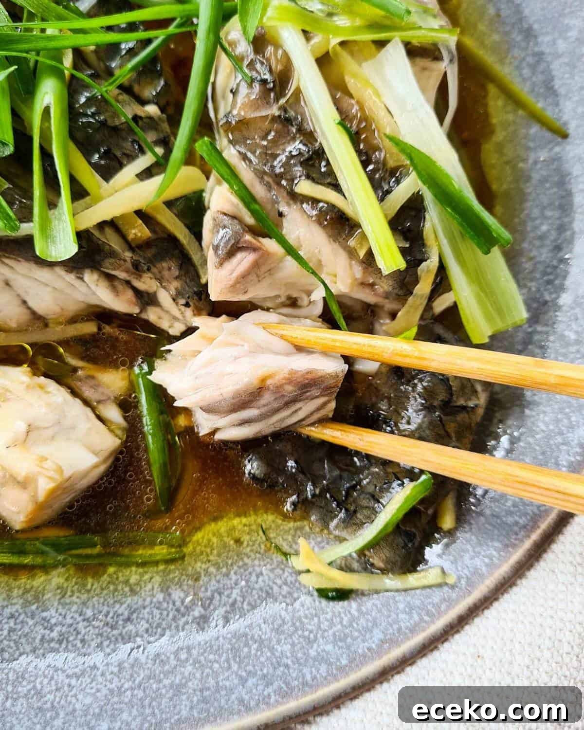 Close up of a piece of cooked Chinese steamed fish being flaked off with a pair of chopsticks