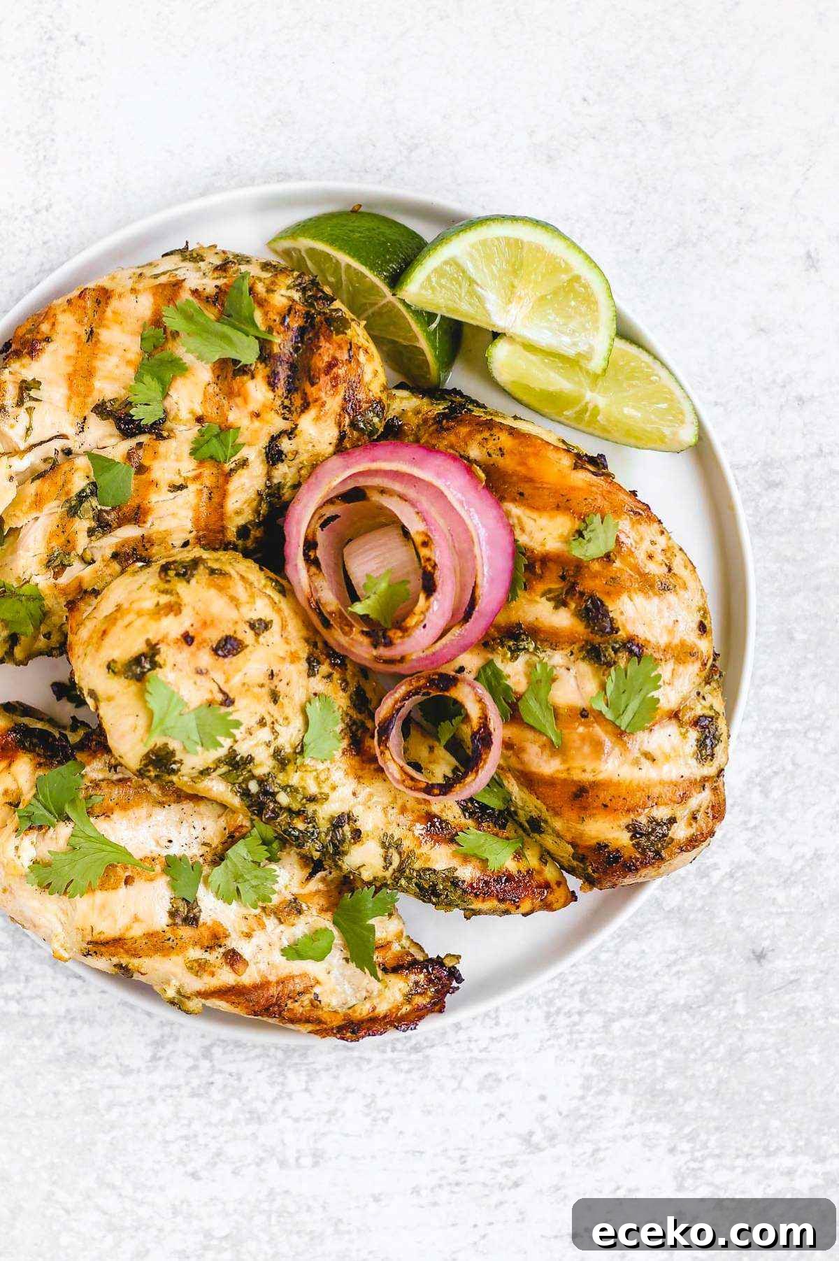 Four grilled cilantro lime chicken breasts with grilled onions and lime slices on a round plate.