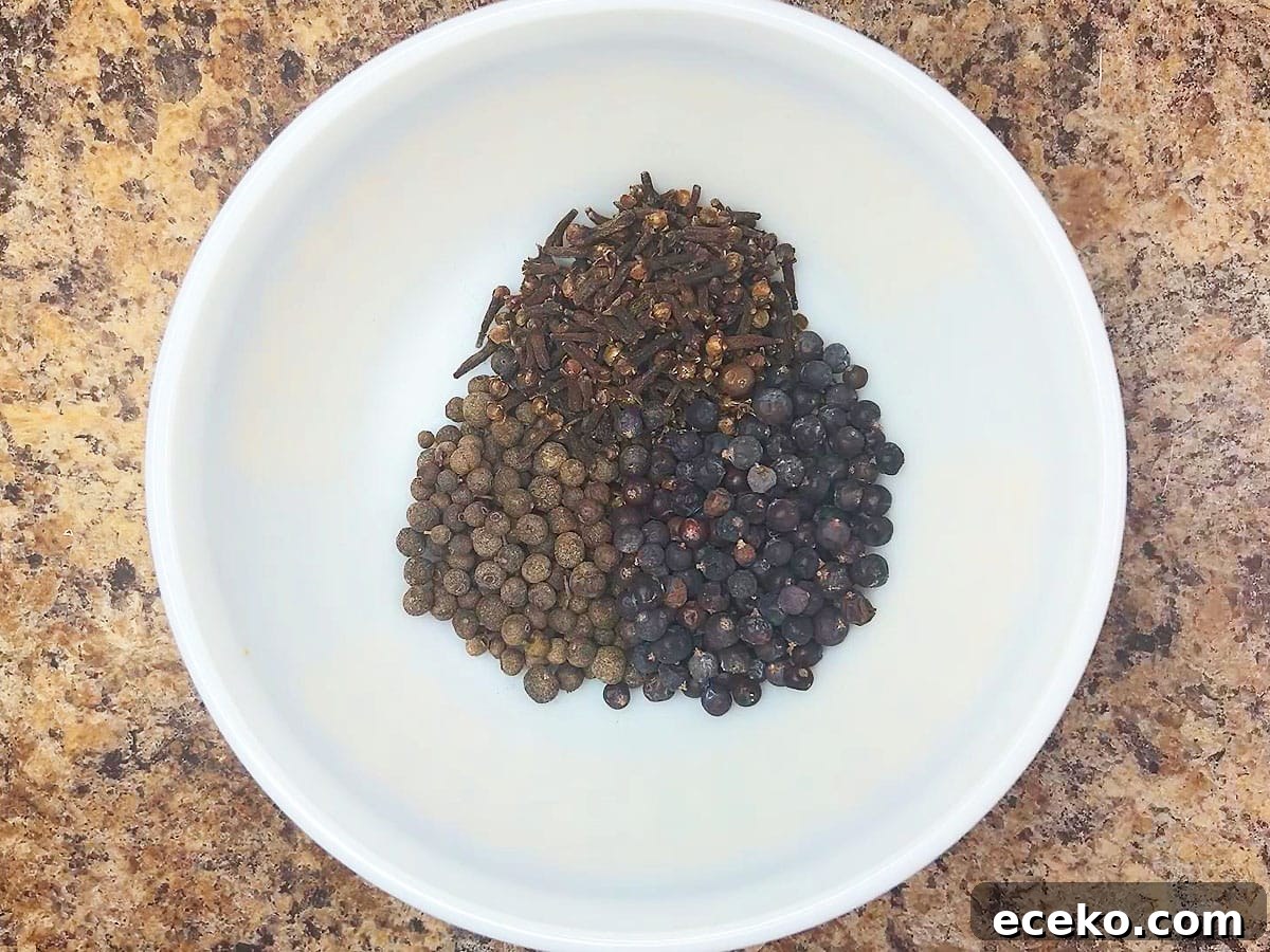 Whole allspice berries, cloves, and juniper berries in a small mixing bowl.