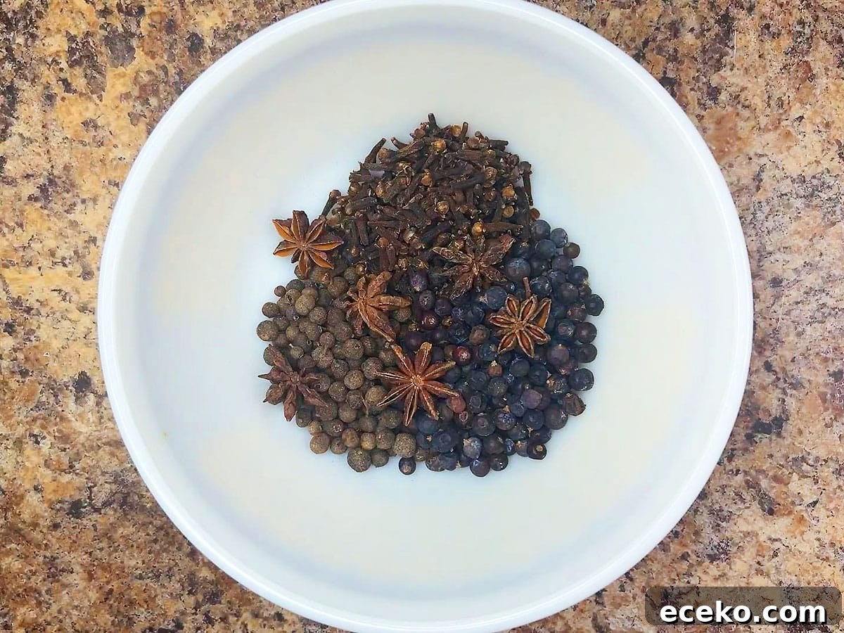 Whole allspice berries, cloves, juniper berries, and star anise in a small mixing bowl.