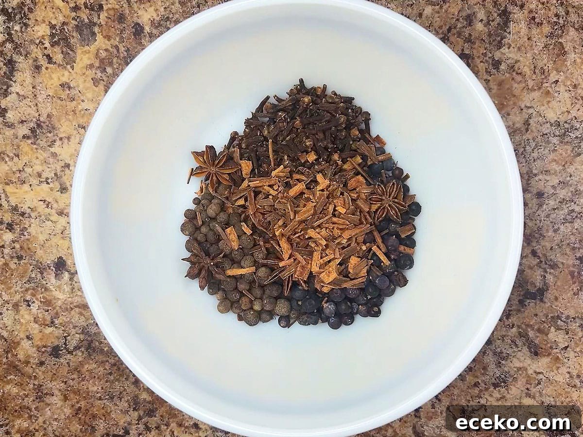 Whole allspice berries, cloves, juniper berries, star anise, and crushed cinnamon sticks in a small mixing bowl.