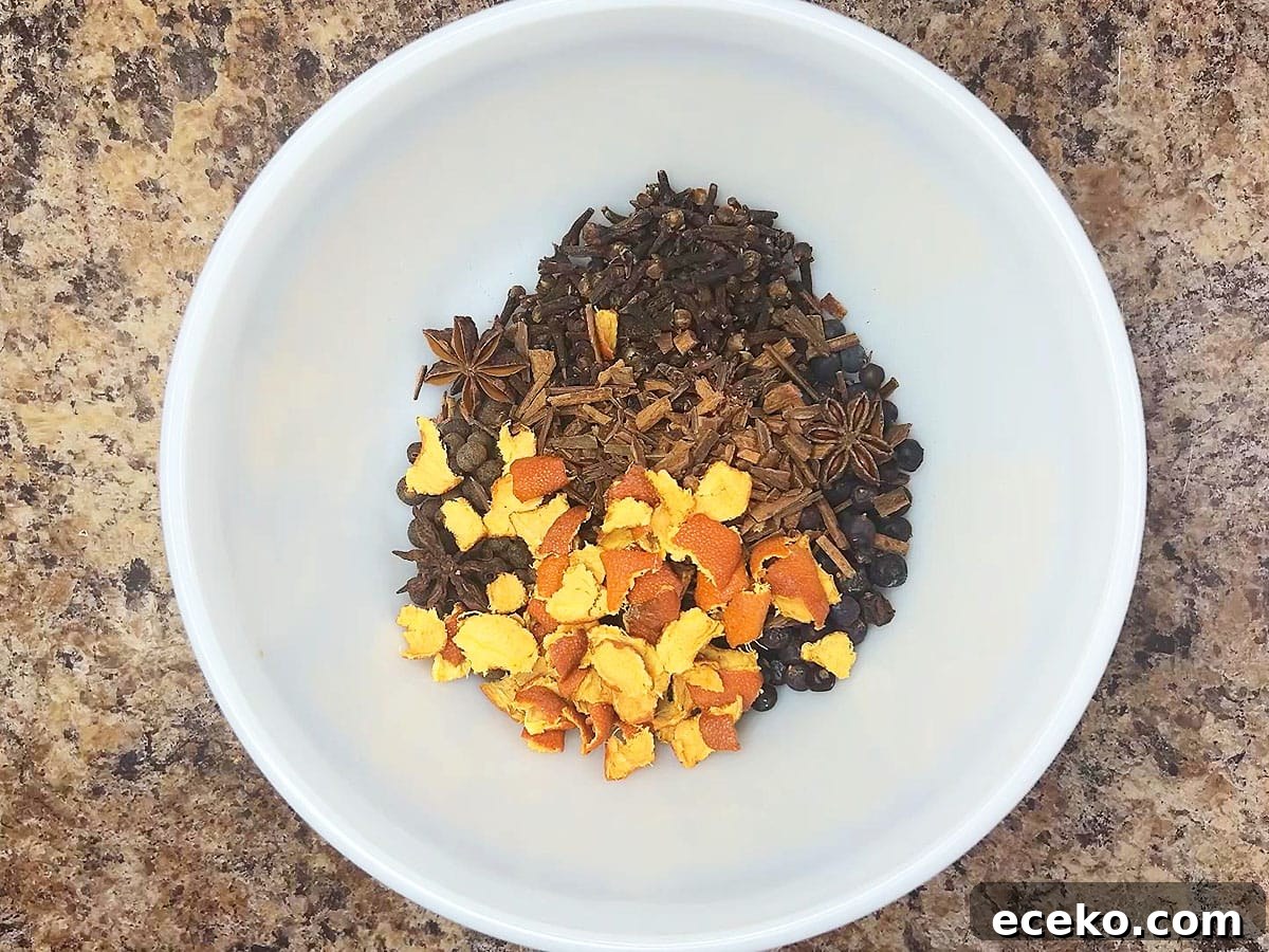 Whole allspice berries, cloves, juniper berries, star anise, crushed cinnamon sticks, and dried orange peel in a small mixing bowl.