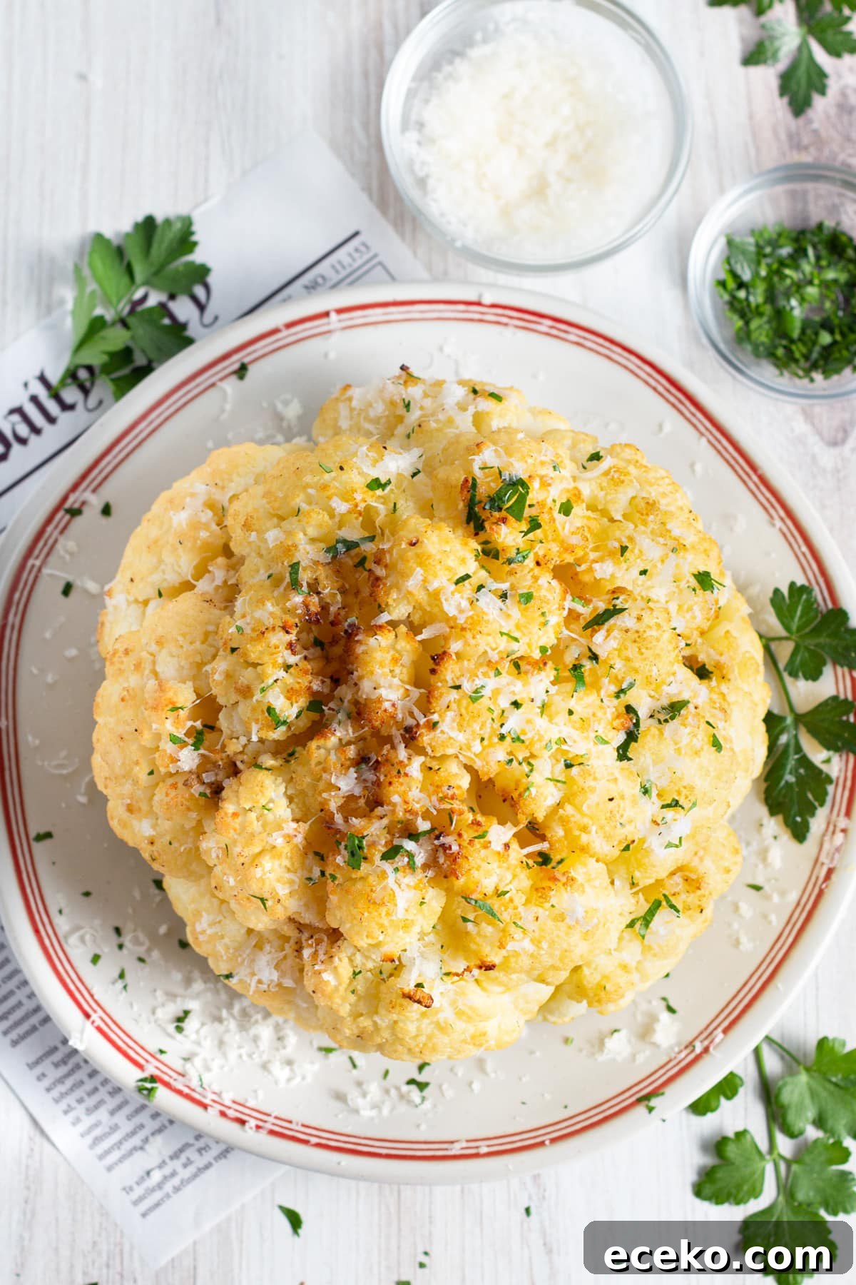 Picture of the cauliflower cooked in a plate with bowls of parmesan and parsley. 