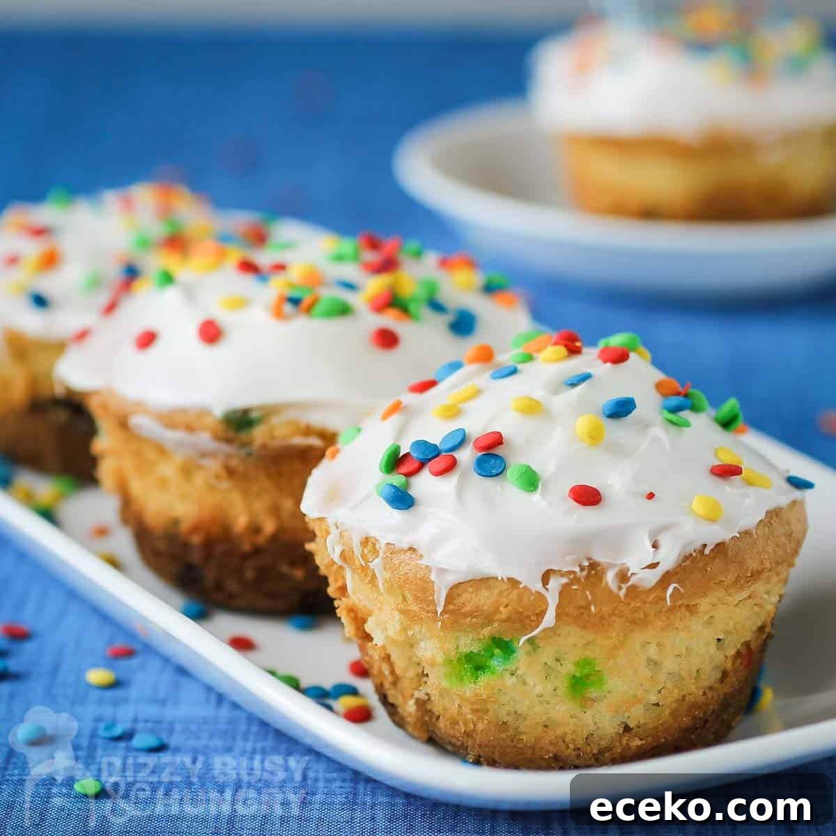 Funfetti Oreo Cupcakes: Simple, Colorful Party Treat 6 Side shot of three cupcakes on a white rectangle plate on a blue tablecloth with more cupcakes in the background.