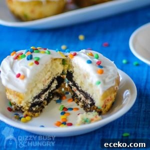 Funfetti Oreo Cupcakes: Simple, Colorful Party Treat 7 Side close up shot of a cupcake split in half on a small white plate with more cupcakes in the background all on a blue tablecloth.