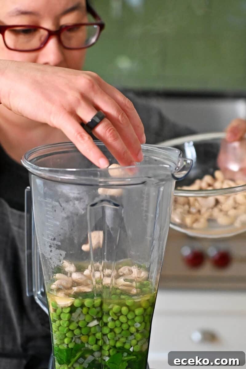 Adding drained cashews to a Vitamix filled with pea soup ready to be blended