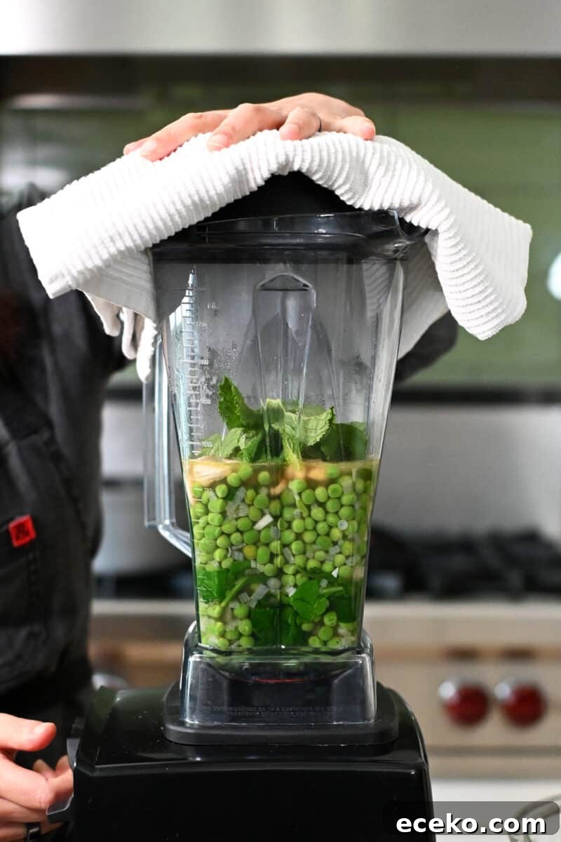 Side view of a Vitamix blender filled with pea soup ingredients.