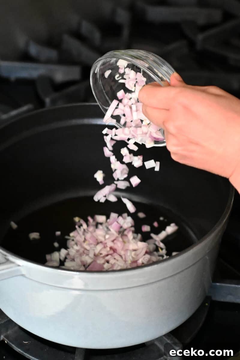A bowl of chopped shallots is being poured into a gray dutch oven to make pea soup