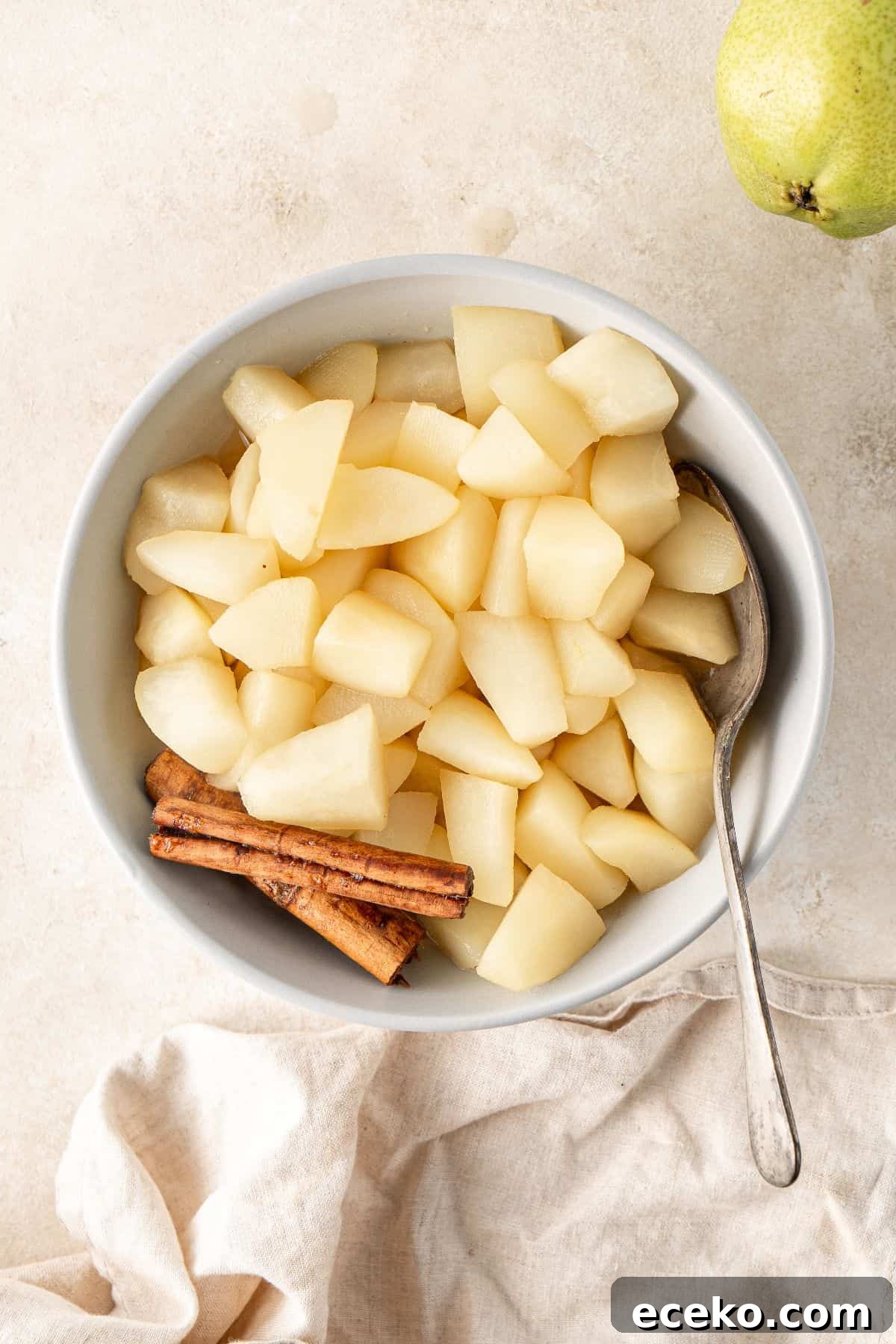 Round bowl of Stewed Pears, with two cinnamon sticks and a spoon sitting in bowl.