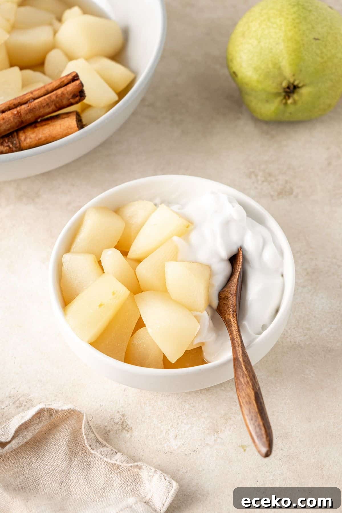 A small bowl with a serve of Stewed Pears and some coconut yoghurt on the side, with a wooden spoon.
