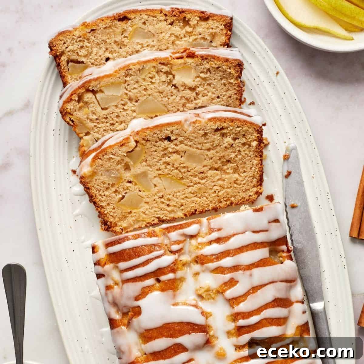 Pear Loaf Cake, with three slices cut, sitting on a white oval platter, with a knife on the side.