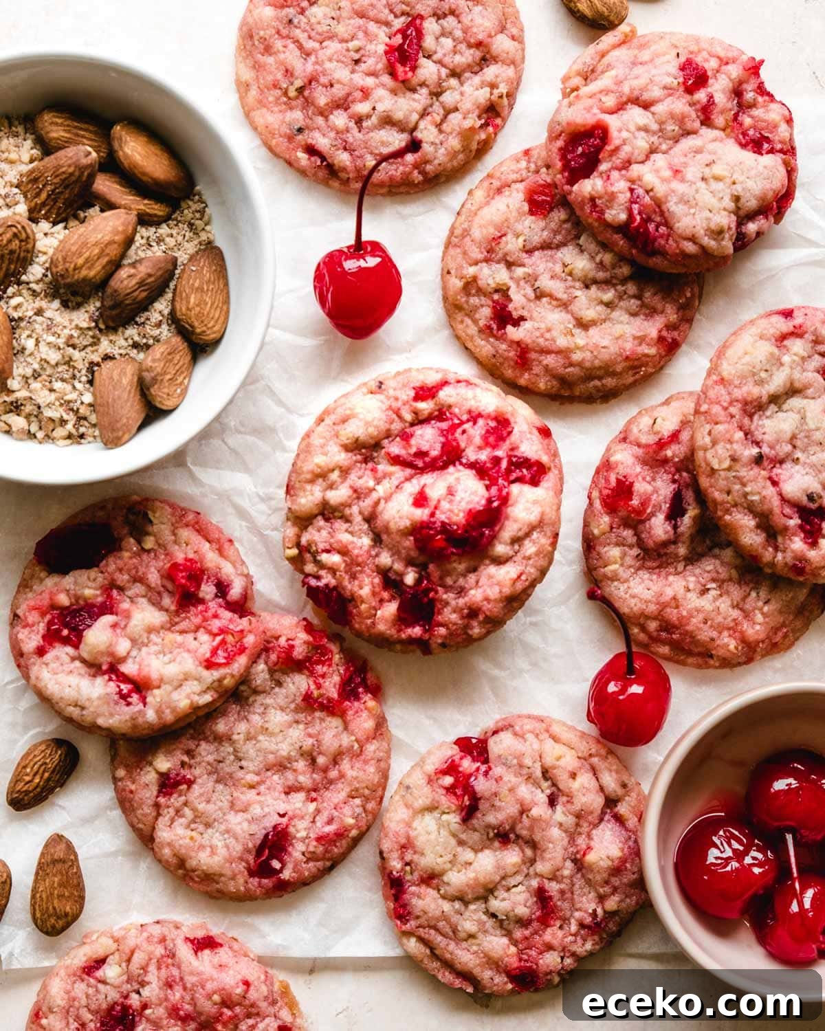 Chewy Cherry Almond Cookies with White Chocolate Chunks 7 Almond cherry cookies on a piece of parchment paper with almonds and maraschino cherries around.