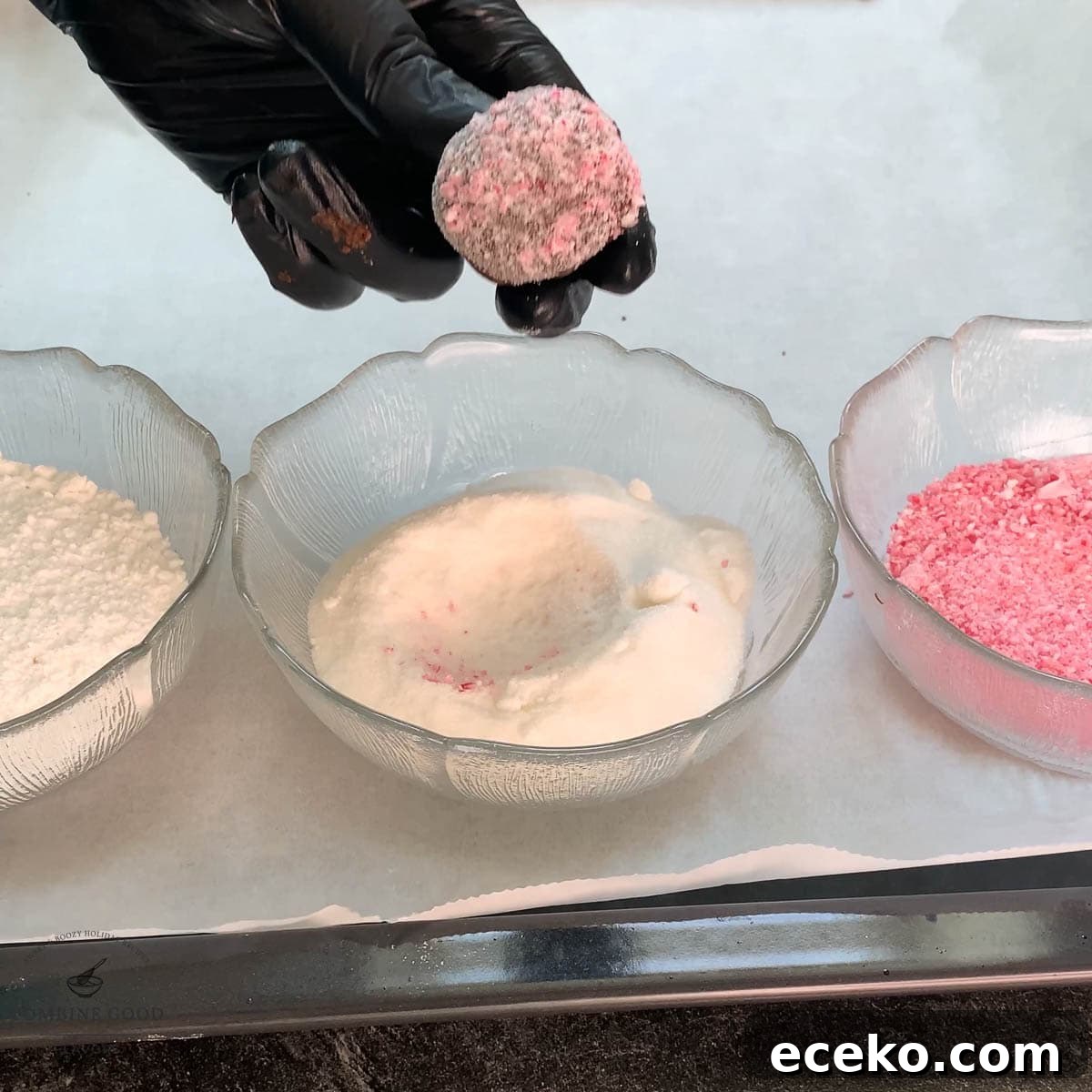 Chocolate Peppermint Crinkle Cookies Recipe for the Holidays 14 Hand with black gloves holding dough ball over a bowl filled with granulated sugar.