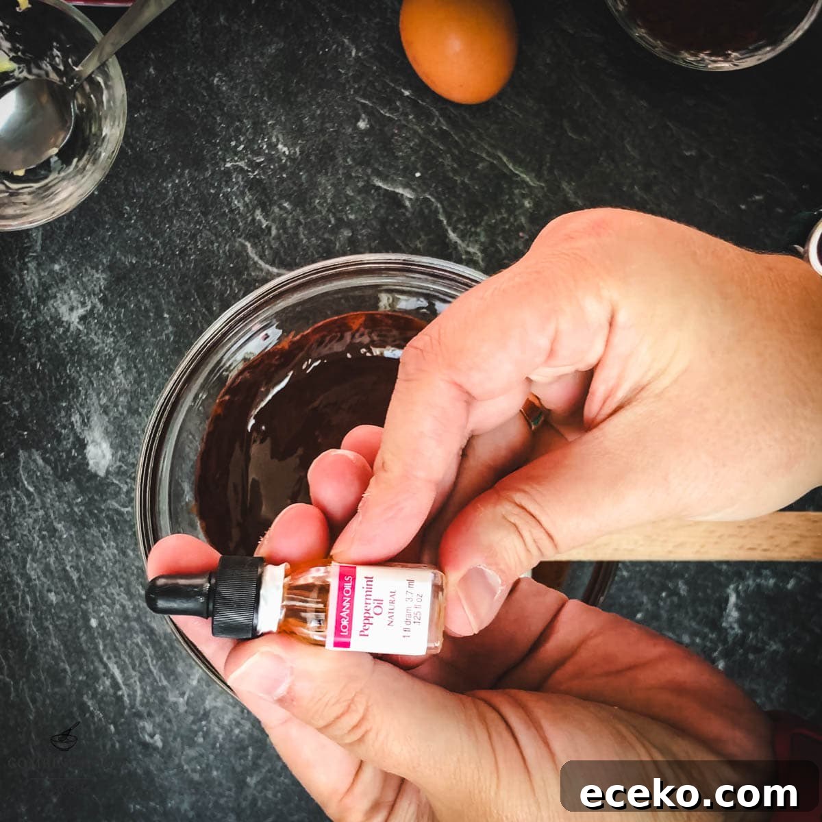 Chocolate Peppermint Crinkle Cookies Recipe for the Holidays 8 Hands holding peppermint oil over a bowl of melted chocolate.