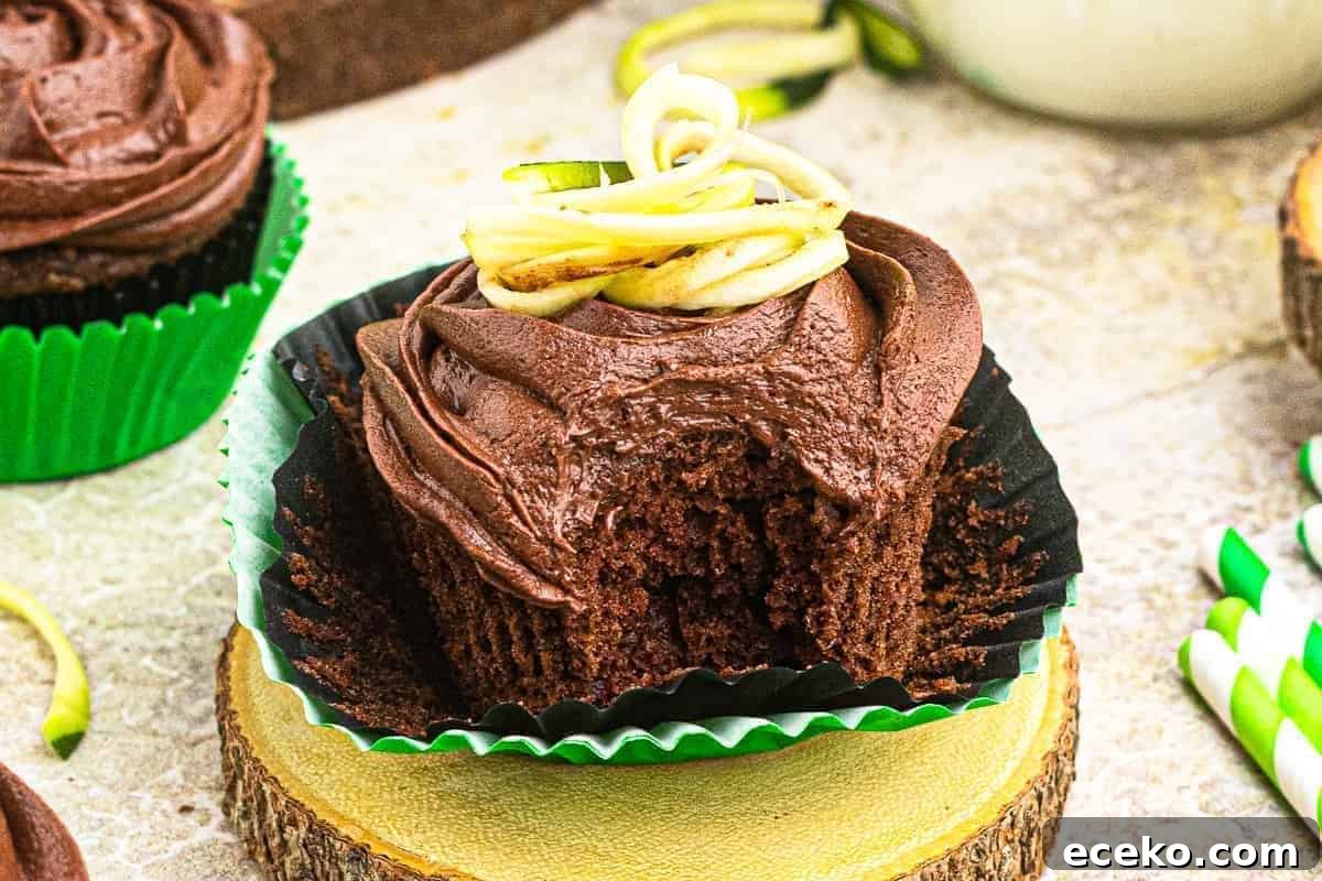 an unwrapped and bitten frosted chocolate zucchini cupcake with shredded zucchini on top.