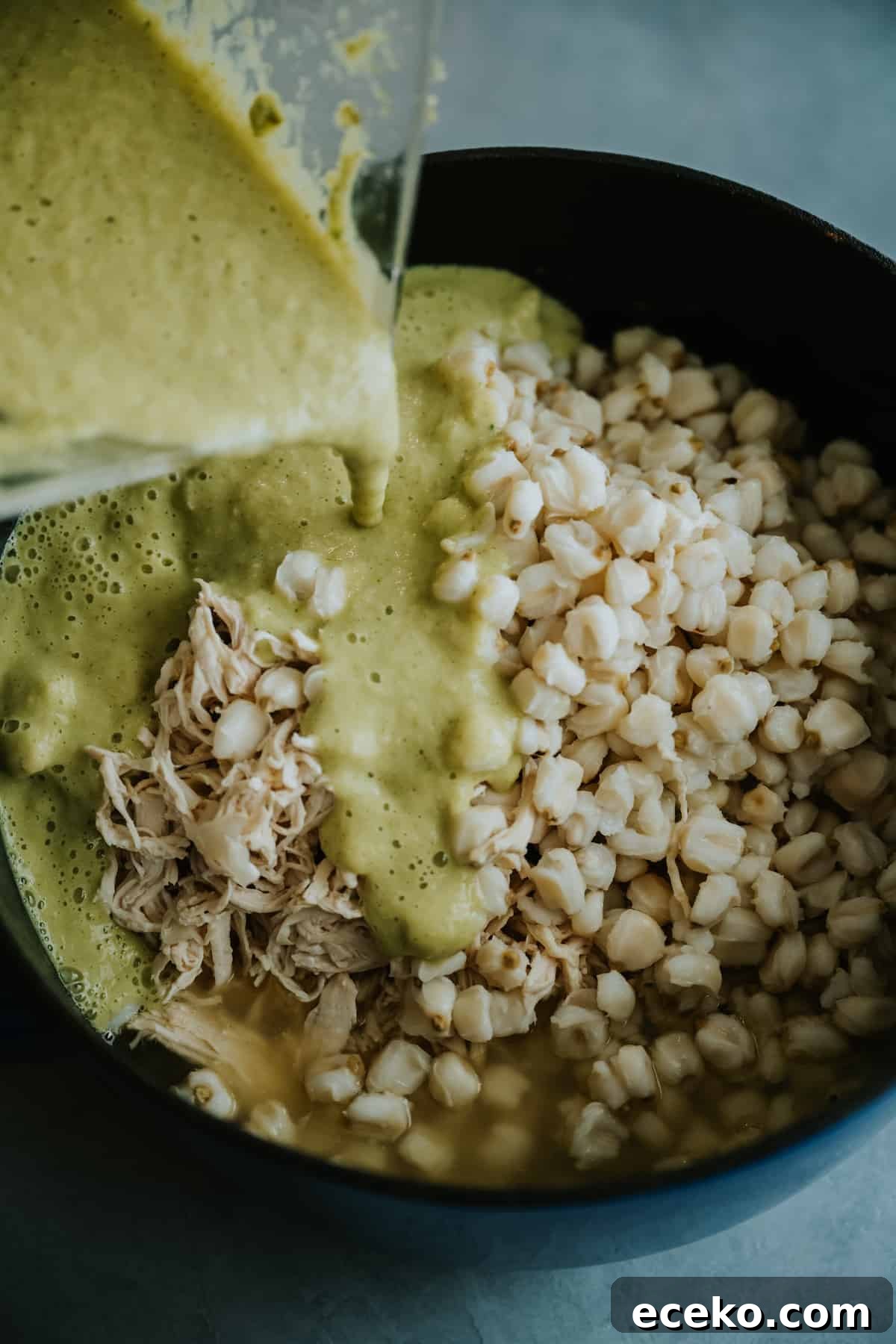 salsa verde, poached chicken, and drained hominy being poured into a stock pot. 