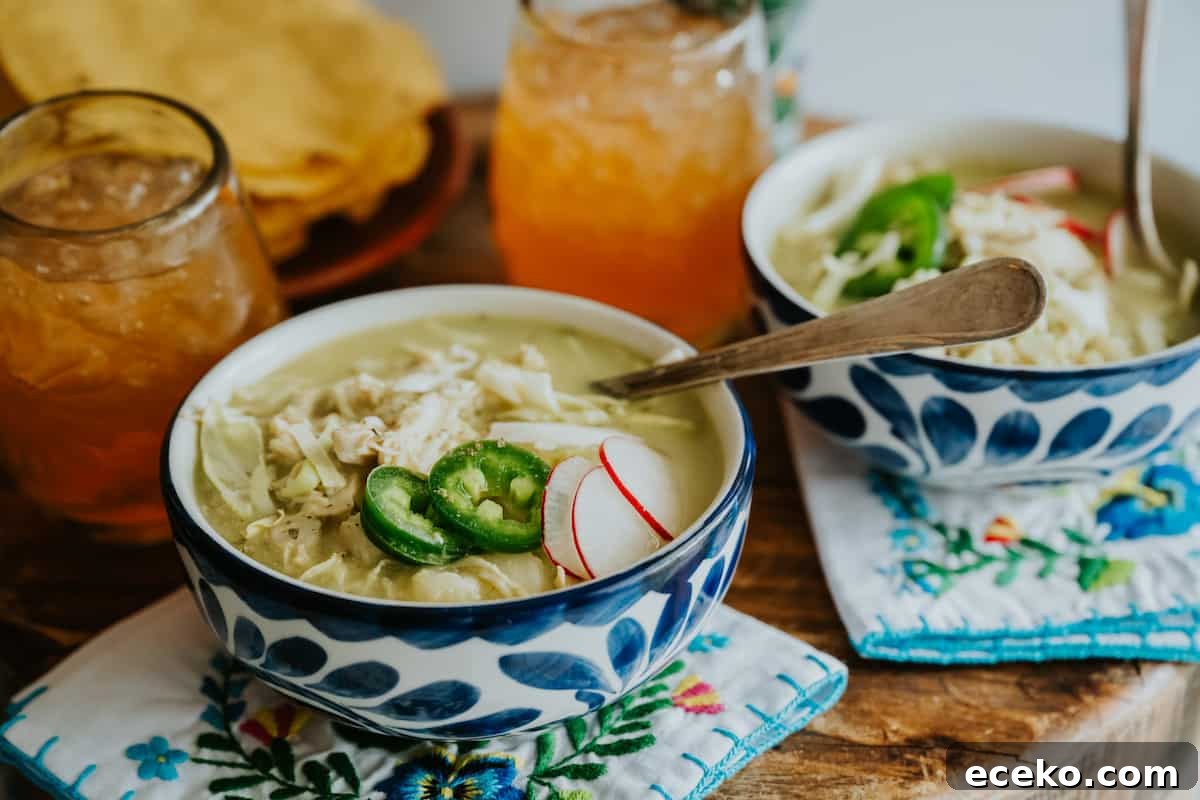 table with two blue and white hand painted bowls filled with chicken pozole verde topped with an assortment of garnishes, two stemless wine glasses filled with iced tea, and a plate of crispy tosada shells for serving alongside the posole.