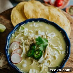 navy blue bowl filled with chicken pozole verde topped with jalapeno and radish slices, shredded lettuce, and fresh cilantro leaves.
