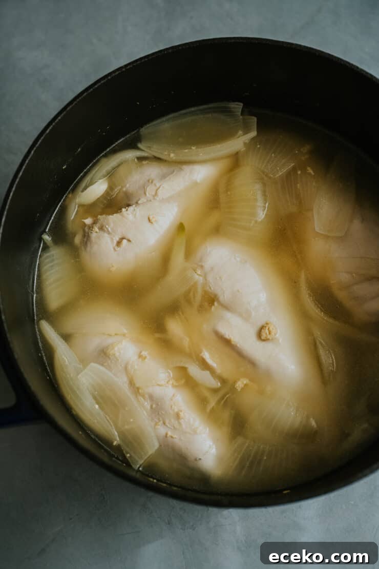 poached chicken breasts in the pot with cooked onions and garlic.