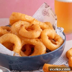 A bowl of gluten free onion rings with a pint of gluten free lager in the background.