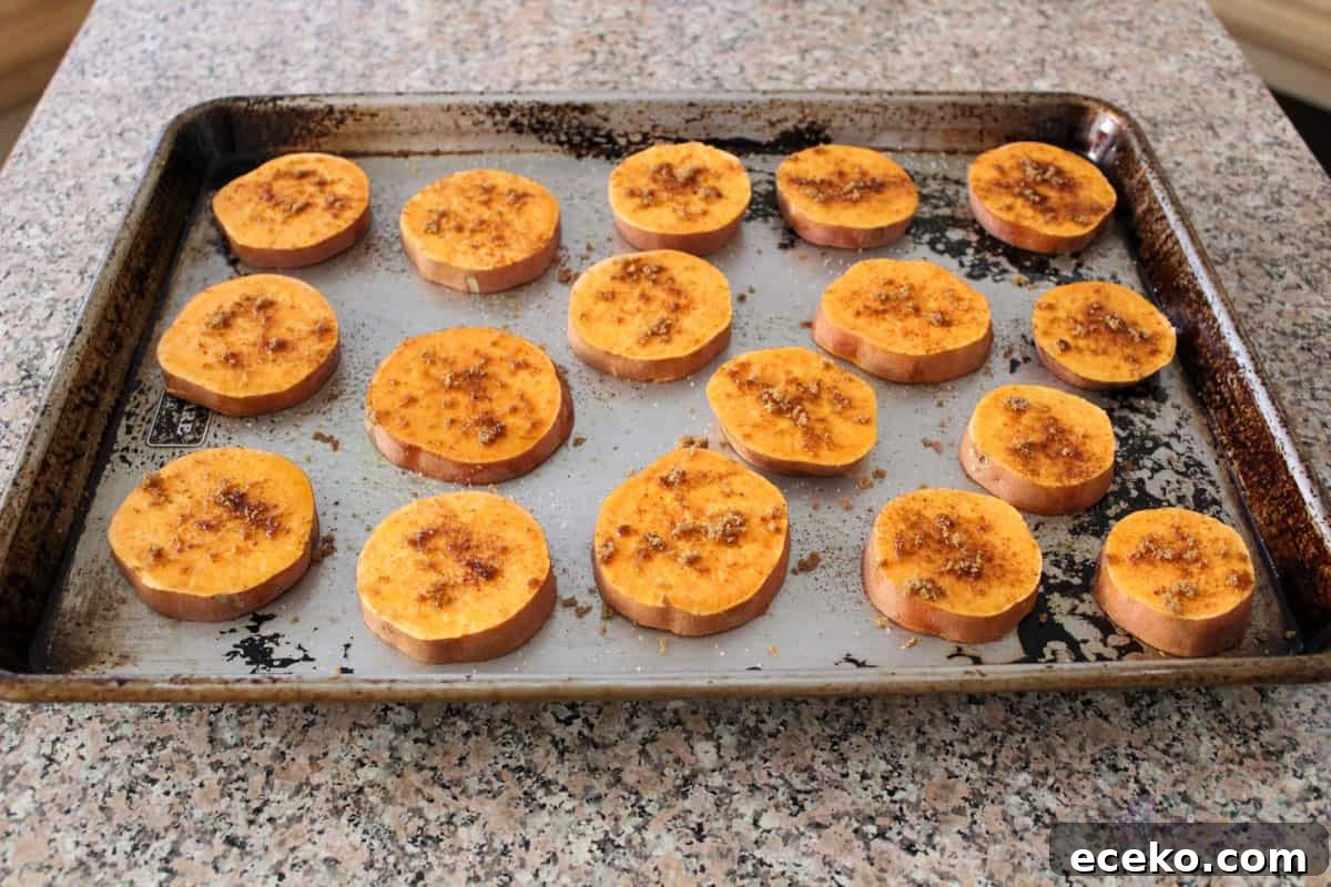 Sweet potato slices on a baking sheet and seasoned, ready for the oven.