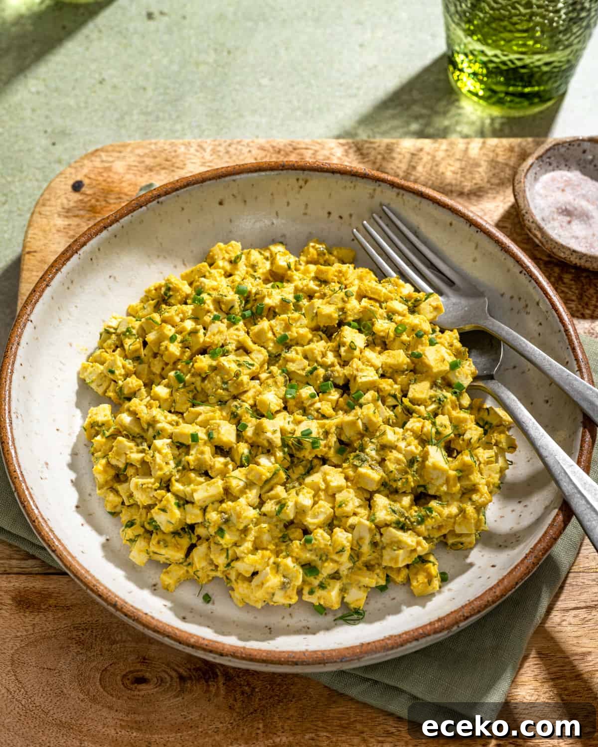 Vegan egg salad in a large white bowl on a wooden cutting board.