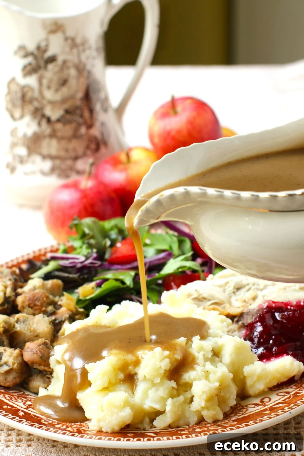 Pouring apple cider gravy onto a pile of mashed potatoes on a fully loaded plate of turkey dinner.