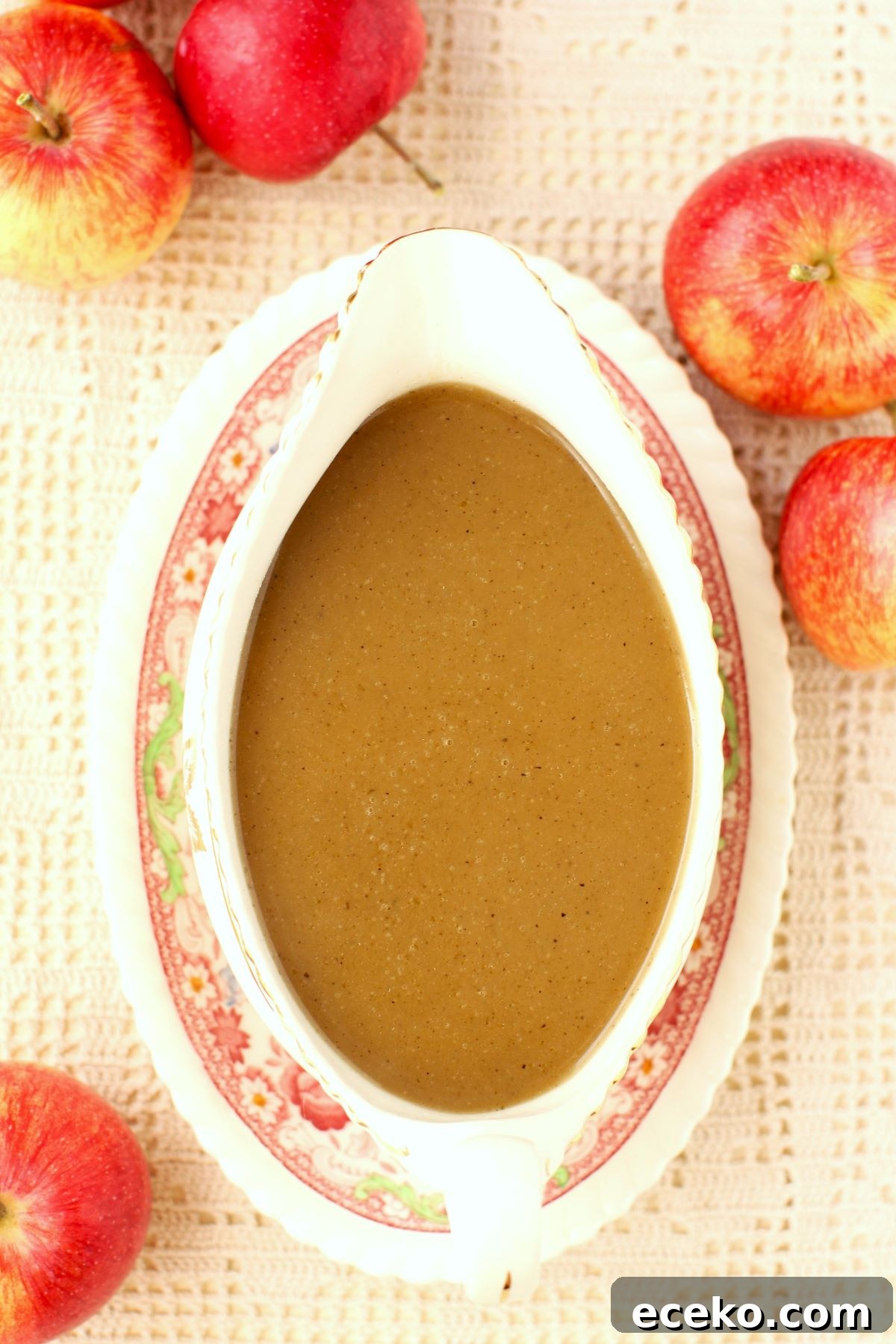 Top down view of a gravy boat filled with apple cider gravy, a few apples beside it.