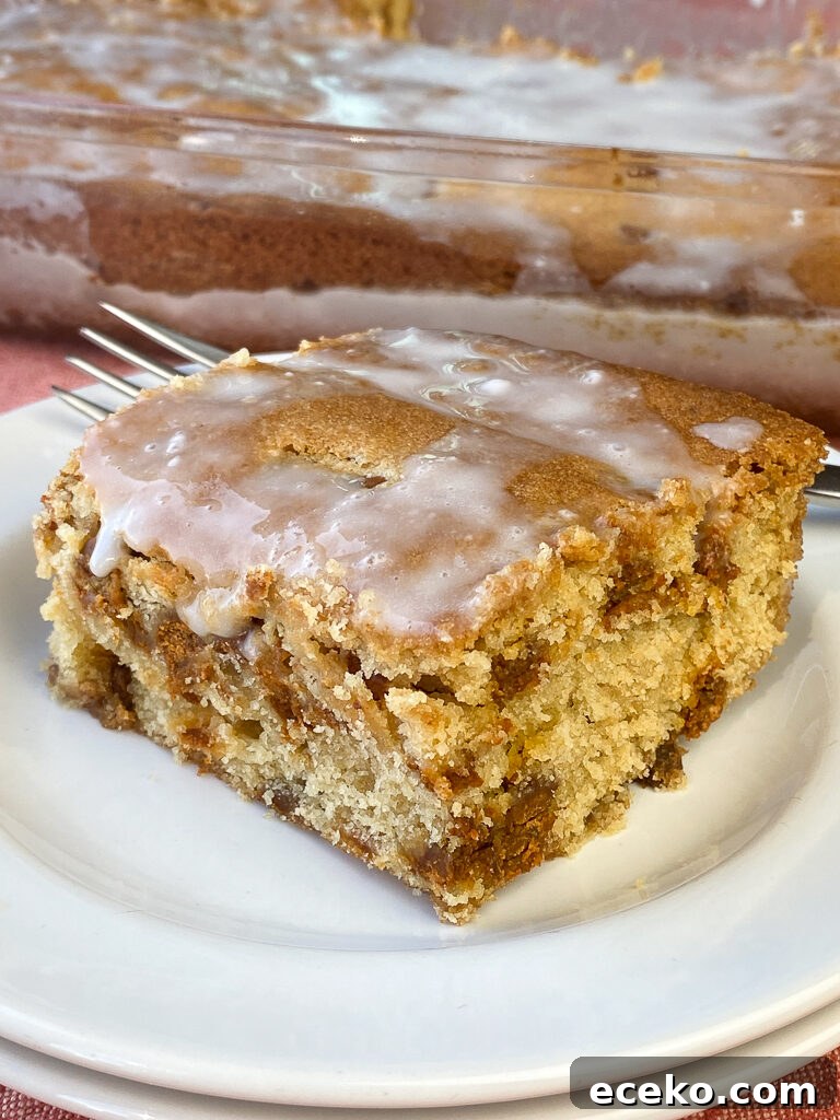 Cinnamon Applesauce Cake Recipe with Moist Spice and Quick Prep 6 Moist piece of applesauce coffee cake with a powdered sugar icing sitting on a stack of white plates with a fork and baking dish full of coffee cake in the background