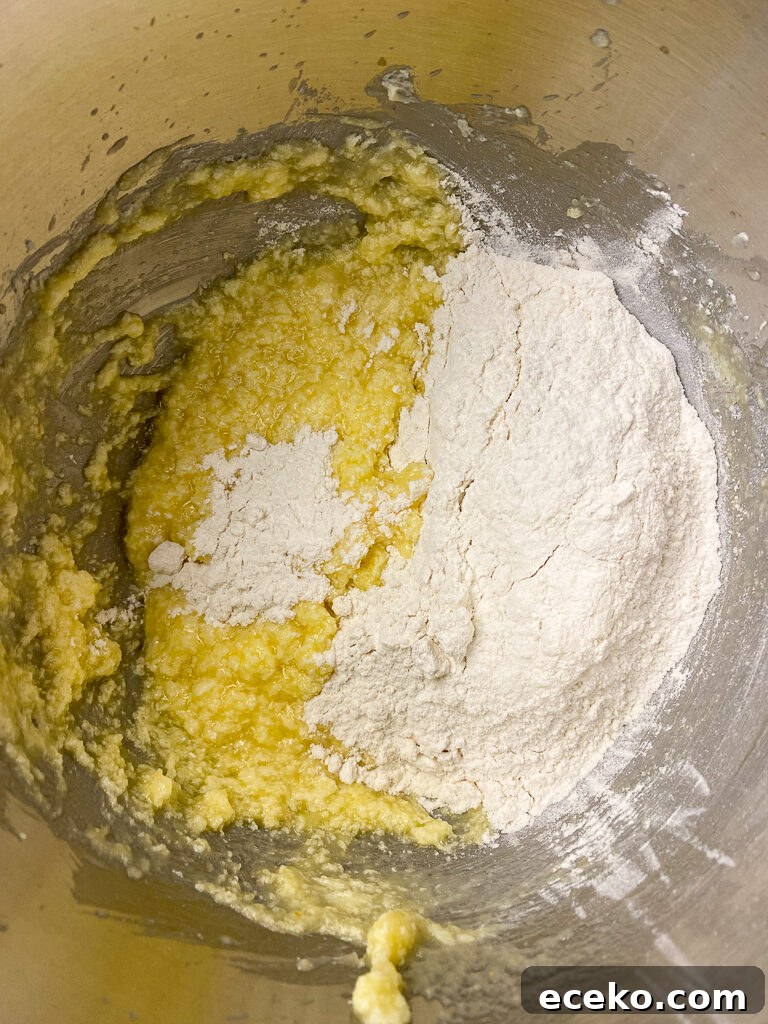 Cinnamon Applesauce Cake Recipe with Moist Spice and Quick Prep 9 Flour being added to applesauce, sugar, butter and eggs mixture in a metal mixing bowl
