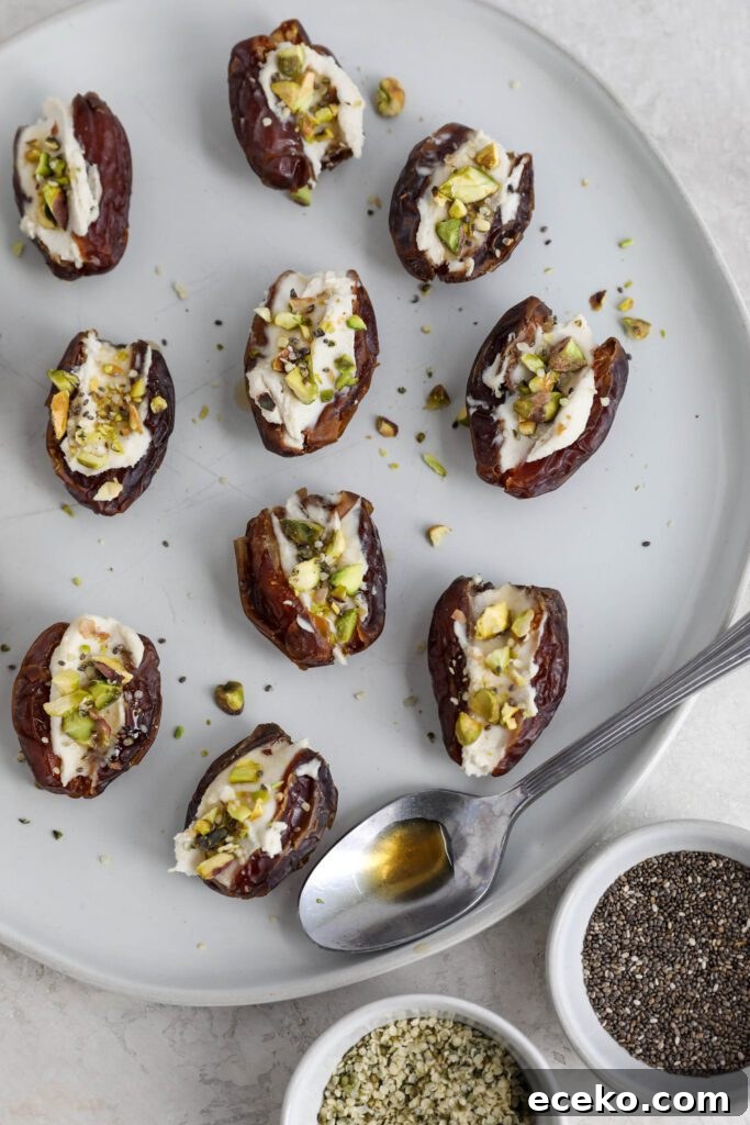 Dates stuffed with cream cheese and topped with pistachios, hemp hearts, and chia seeds on white plate