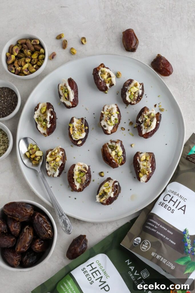Dates stuffed with cream cheese and topped with pistachios, hemp hearts, and chia seeds on white plate