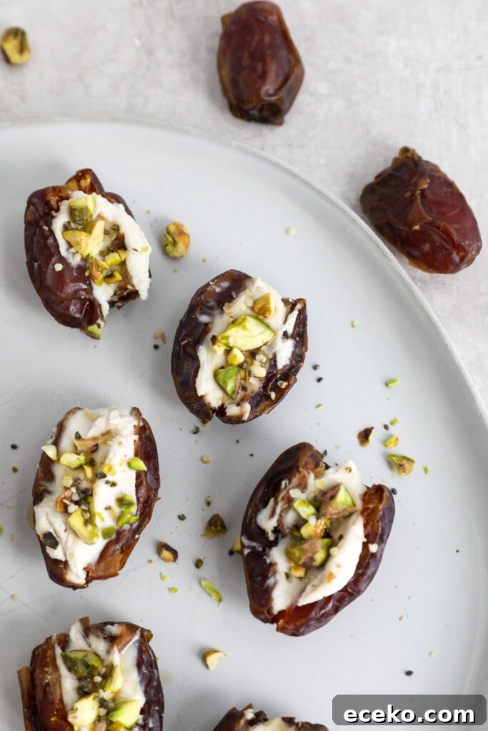Dates stuffed with cream cheese and topped with pistachios, hemp hearts, and chia seeds on white plate