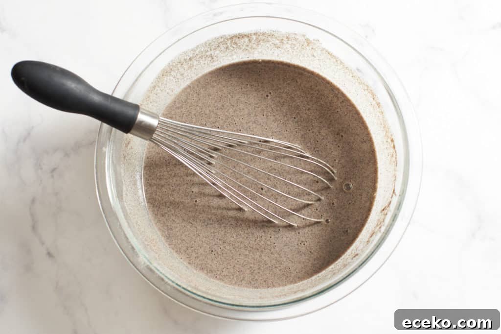 A whisk in a glass bowl of buckwheat crepe batter.