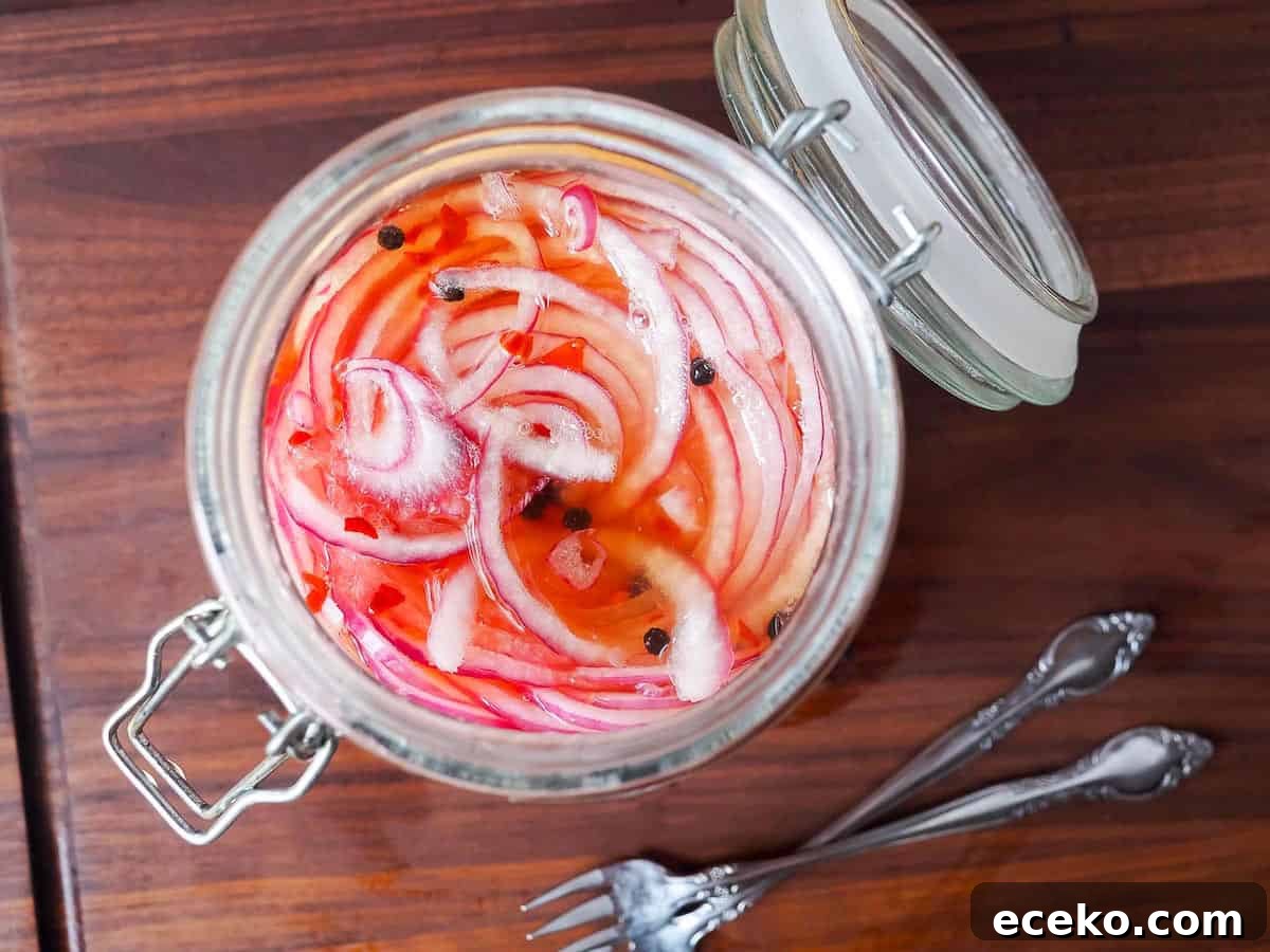 Quick Pickled Red Onions Recipe for Toppings & Salads 7 A glass jar with pickled red onions in it and two small forks on the side.