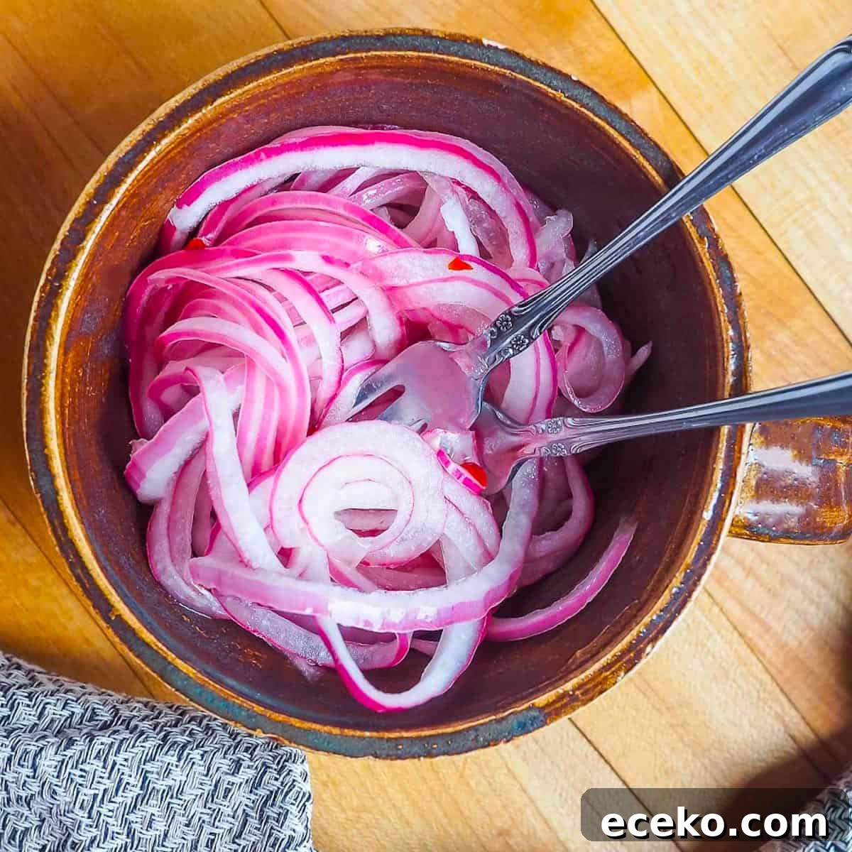 Quick Pickled Red Onions Recipe for Toppings & Salads 8 A small brown mug with pickled red onions and two small forks twisted in the onions.