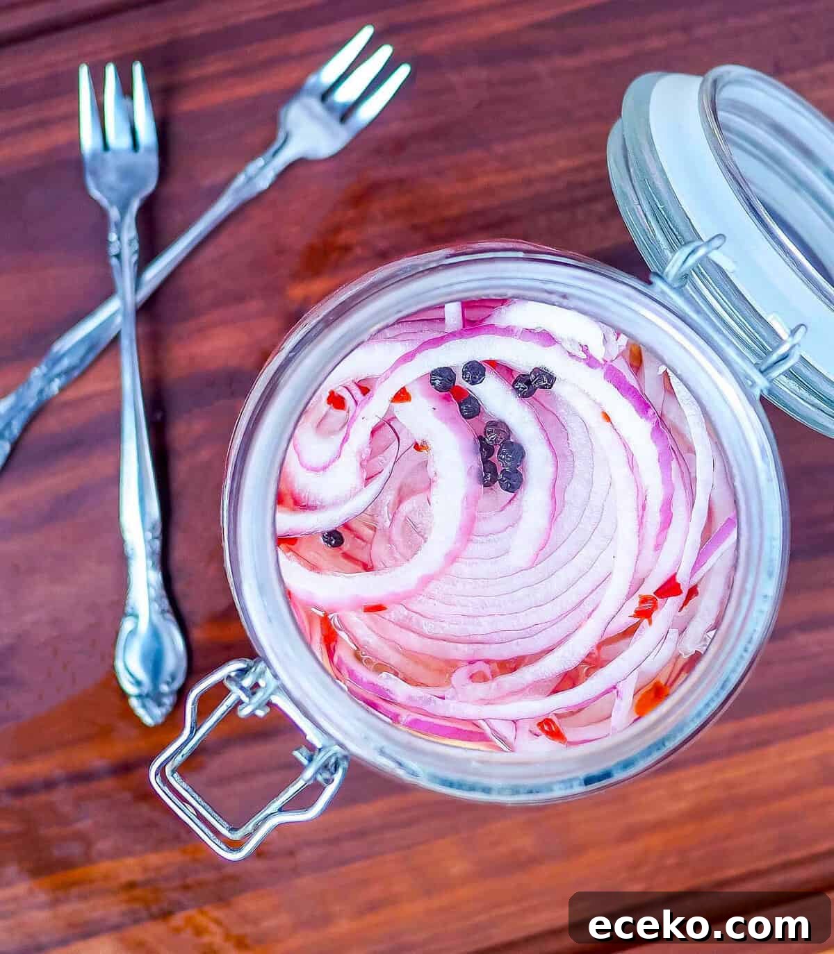 Quick Pickled Red Onions Recipe for Toppings & Salads 9 A jar of pickled red onions with peppercorns and two small forks.